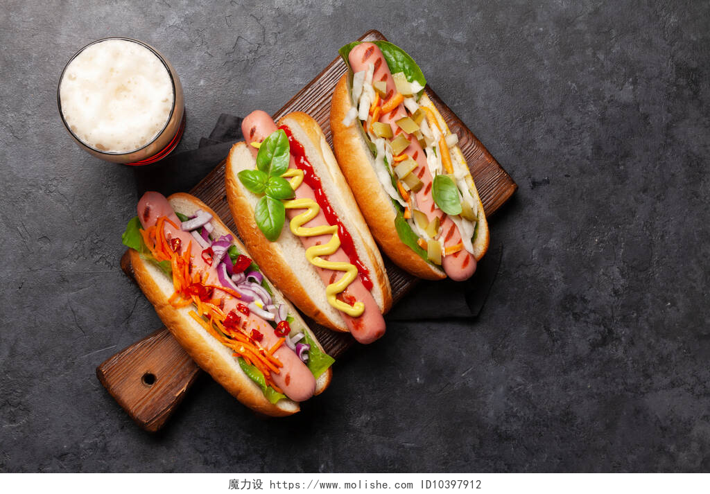 俯拍石板上的三明治各种热狗，蔬菜、生菜、调味品和啤酒杯，背景为石材。带有复制空间的顶部视图。平躺在床上